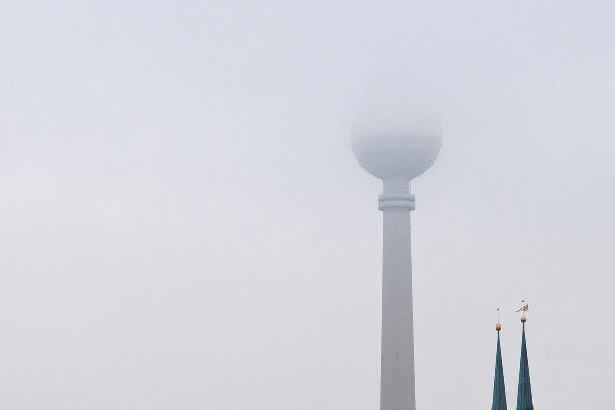 Eine Abbildung des Berliner Fernsehturm steht im Berliner Ortsteil Mitte, nahe dem Alexanderplatz, und ist mit 368 Metern das höchste Bauwerk Deutschlands sowie das vierthöchste freistehende Bauwerk Europas. Er war im Jahr der Fertigstellung 1969 der zweithöchste Fernsehturm der Welt und zählt mit über einer Million Besuchern jährlich zu den zehn beliebtesten Sehenswürdigkeiten in Deutschland. In diese Foto ist der obere Teil der Fernsehturm halb bedeckt von grauen Wolken.