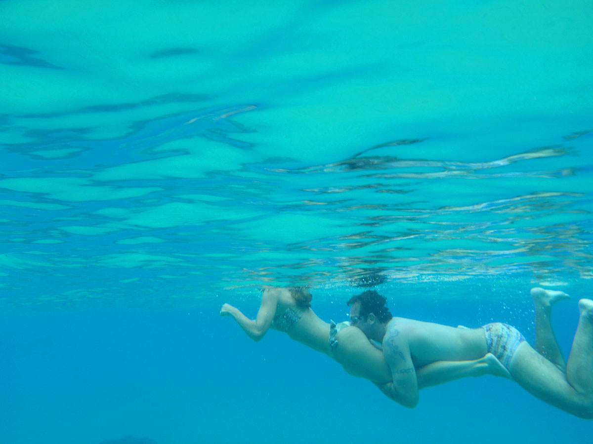 Ein Man schwimmt mit dem Kopf zwischen die Beine seine Partnerin. Das bild wurde Unterwasser aufgenommen, das Wasser ist türkisblau. Das Foto wurde in Fernando de Noronha, Brasilien aufgenommen.